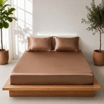 Light brown satin bedsheet with two matching pillow covers neatly arranged on a wooden platform bed in a bright, minimalist bedroom