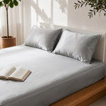 Silver grey satin bedsheet with matching pillow covers styled on a wooden bed with an open book