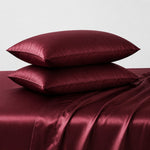 Maroon satin pillowcases on a matching satin sheet set against a light gray background