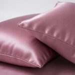 Two soft, shiny pink satin pillows are stacked on each other, conveying a luxurious and comforting feel against a neutral background.