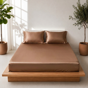 Light brown satin bedsheet with two matching pillow covers neatly arranged on a wooden platform bed in a bright, minimalist bedroom