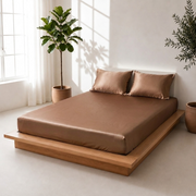 Angled view of a toffee satin bedsheet with matching pillow covers on a wooden platform bed beside indoor plants