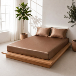 Angled view of a toffee satin bedsheet with matching pillow covers on a wooden platform bed beside indoor plants