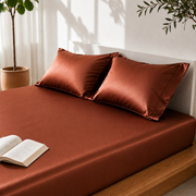 Brown satin sheet set on a bed with an open book and plants in the background.