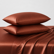 Pair of brown satin pillows on a matching satin sheet set against a light gray background