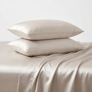 Two cream colored satin pillows on a satin sheet with a plain background