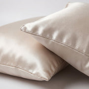 Two cream satin pillows on a light background