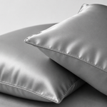 Two satin pillowcases in a light gray color, stacked on a matching gray background.