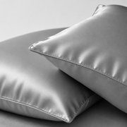 Two satin pillowcases in a light gray color, stacked on a matching gray background.