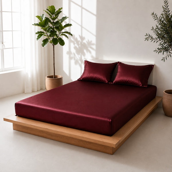 Bed with maroon bedding and pillows in a bright room with plants