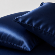 Two navy blue satin pillowcases stacked on a matching navy blue sheet against a light gray background.