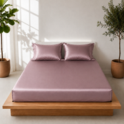 A luxurious bed adorned with Milano Soft Satin rose color sheets, complemented by a stylish plant in the corner.