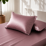 Two pink satin pillows on a matching pink bedspread with a plant in the background.