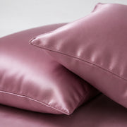 Two soft, shiny pink satin pillows are stacked on each other, conveying a luxurious and comforting feel against a neutral background.