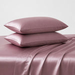 Pink satin pillowcases on a matching pink satin sheet set against a light gray background
