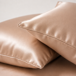 Two champagne satin overlapping pillows. The smooth shiny fabric gives them a luxurious and cosy feel.