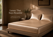 A bed dressed in shiny champagne-gold satin sheets and matching pillowcases in a warmly lit bedroom. Text on the left reads, 'Luxury That Stays Beautiful' with smaller descriptive copy below.