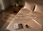 A bed dressed in shiny champagne-colored satin bedding with two matching pillowcases, styled in a warm bedroom scene with a wooden nightstand, curtains, and overlaid text reading 'Made For Slow Mornings'.