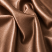 A close-up of draped satin fabric in a warm metallic bronze color, showing soft folds and a glossy sheen.